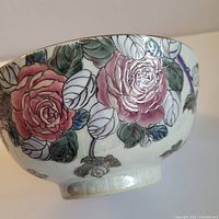 Close-up side view of the porcelain bowl showing detailed hand painted floral rose designs in pink, red, and green hues with a cloisonne style outline.