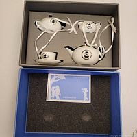 Four piece Wedgwood White Cameo teaset ornaments in original box including teapot, sugar bowl, creamer, and teacup with saucer, all with white ribbons for hanging.