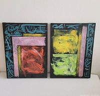 Front view of two original acrylic abstract paintings by Andrew Mackie. The paintings display bold colors and abstract geometric shapes with calligraphic blue decorations on black backgrounds.