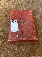 Closed red textured case holding antique flatware set with MaxSold tag.