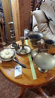 Photo showing the full set of brass items on a wooden table, including candle holders, footed bowls, a vase, and a pot with wooden handle.