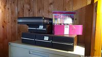 Stack of black CD storage cases and pink box on filing cabinet