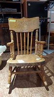 Front facing view of the vintage child's wooden rocking chair showing carved press back and turned spindle arms and legs.