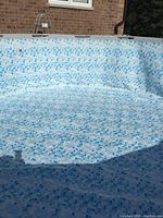 Photo of empty above ground pool showing blue and white mosaic liner with a few pool ladder rungs visible outside.