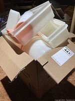 Box containing multiple white and translucent plastic containers with lids, some lids peach colored.