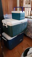 Three coolers stacked indoors - small Igloo cooler on top, green cooler in the middle, and blue cooler on the bottom.