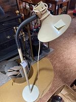 Full view of the floor lamp showing gooseneck arm, round flat base, and conical lampshade with an off-white color.