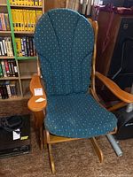 Wooden glider rocker with blue cushion featuring white dot pattern, wooden frame and armrests, visible wear and need for cleaning.