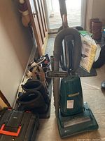 Green Kenmore upright vacuum cleaner standing on floor with shoes and bags nearby.