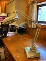 Magnifying lamp on wooden desk with swing arm extended, showing electrical cord and weighted base.
