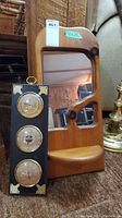 Two-item lot showing wood framed mirror with small shelf beside the leather framed weather station vertically positioned on carpet.