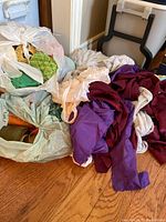 Photo showing several large pieces of fabric and multiple skeins of crochet cotton thread in plastic bags on a wooden floor.