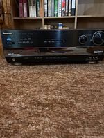 Front view of the Panasonic AV Control Receiver showing power button, input controls, and headphone jack.