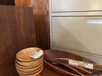 Stack of six light wooden salad bowls next to large dark wooden serving bowl and a pair of wooden salad serving utensils.