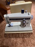 Full view of Kenmore sewing machine set up with spool of blue thread on top and carrying case behind