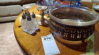 Photo showing four glass salt and pepper shakers with silver tops, two silver candle holders, and a large silver bowl on a wooden table.