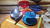 Two footed glass bowls (red and blue), blue ceramic two-tiered dessert tray, and silver-colored metal serving dish on wooden table