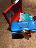 Closed metal blue box with two Lady Stitcher branded boxes behind it.