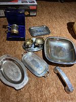 Overview of silver plated shelving trays, cream and sugar set on oval tray, square bowl, small tray, silver mug in case, and a handle.