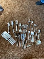 Full collection of multiple silver plate flatware pieces including knives, forks, spoons, and serving pieces laid out on carpet showing condition and variety.
