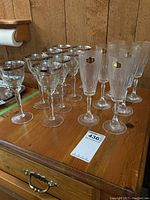 Lot of 15 clear stemware glasses arranged on wooden surface, varying shapes and sizes.