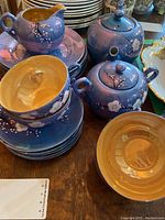 Photo showing stacked plates, cups, cream and sugar containers with a purple exterior and yellow interior, all embossed with white floral designs.