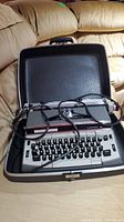 Front view of Eaton Viking Electric 12 typewriter inside black hard carrying case with attached power cord on beige surface.