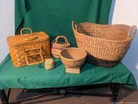 Six varying baskets displayed on green cloth background including large oval basket, rectangular picnic basket, small cubical basket, and round handled baskets
