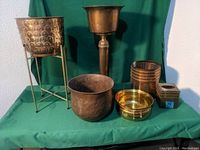Lot of six brass and brass-like items on green cloth background, includes plant stands and pots
