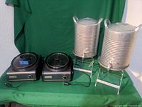 Two black Better Homes crock pots with glass lids and dials alongside two galvanized metal beverage dispensers on stands.