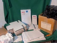 Several stacks of flat white cardboard gift boxes in different sizes and various plastic retail bags including white and black bags, some in a cardboard box and others folded on a table.