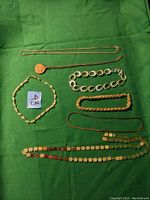 Top view of six gold tone jewelry pieces arranged on green fabric including two necklaces and four bracelets with various link styles and a medallion pendant