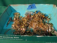 Photo showing the mixed lot of broken and incomplete jewelry items including chains, earrings, beads, and various metal pieces in a blue box.