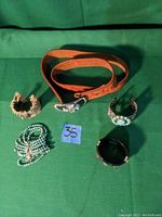 Orange leather belt coiled with various costume bracelets and beaded necklaces arranged around it on green fabric background
