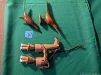 Two long-beaked wooden birds designed for wall mounting, and one terracotta horse wind chime lying on a green cloth background.