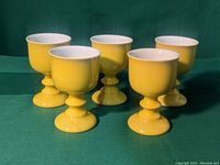 Front view of five yellow pedestal cups with white interiors arranged close together on a green cloth.