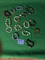 Top-down image of fourteen assorted beaded bracelets on green fabric background, showing arrangement and variety of colors and bead types.