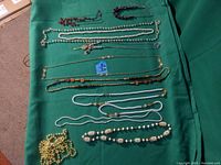 Full view of all necklaces on green cloth showing variety of faux pearls, beads, and chains