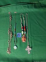 Four necklaces displayed on green fabric, showing detail of cross pendants and beadwork.