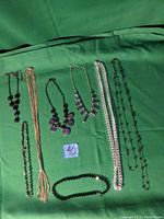 Eight black and silver-tone necklaces displayed on a green surface, ranging from beaded to chain styles with various pendant shapes.