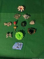 Set of 11 decorative pins arranged on green cloth, showing variety of shapes and colors.