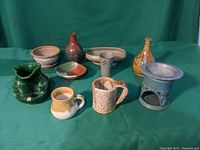Photo showing a variety of pottery items, including pitchers, mugs, bowls, vases, and a candle holder on a green cloth background.