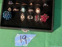 Display of 17 assorted costume rings with various large cluster and floral designs, multiple colors including blue, red, and gold tones.