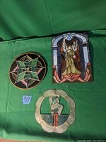 Three decorative pieces on green background: two stained glass panels (an angel and a geometric star) and a mother of pearl bird piece with scalloped edge.