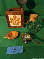 All four tea time items displayed together on green fabric background, showing the wooden utensil holder, glass teapot, metal infuser, and copper strainer.