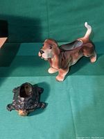 Side and front view of brown and white dachshund dog ceramic planter and dark turtle ceramic planter on green cloth.