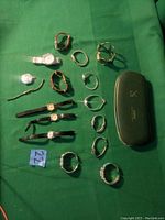 All watches laid out flat on green cloth including wristwatches, cuff watches, pendant watch, and a watch case.