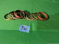 Set of 13 bangles arranged in a line on green fabric background, showing mix of wood and brass materials.