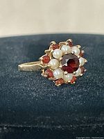 Side view of the 10 kt gold ring showing the garnet center stone surrounded by pearls and smaller garnet stones.