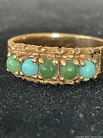 Front close-up showing row of five alternating green and blue cabochon stones set in textured gold band